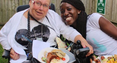 Two women eating food at GIG meeting in a garden.